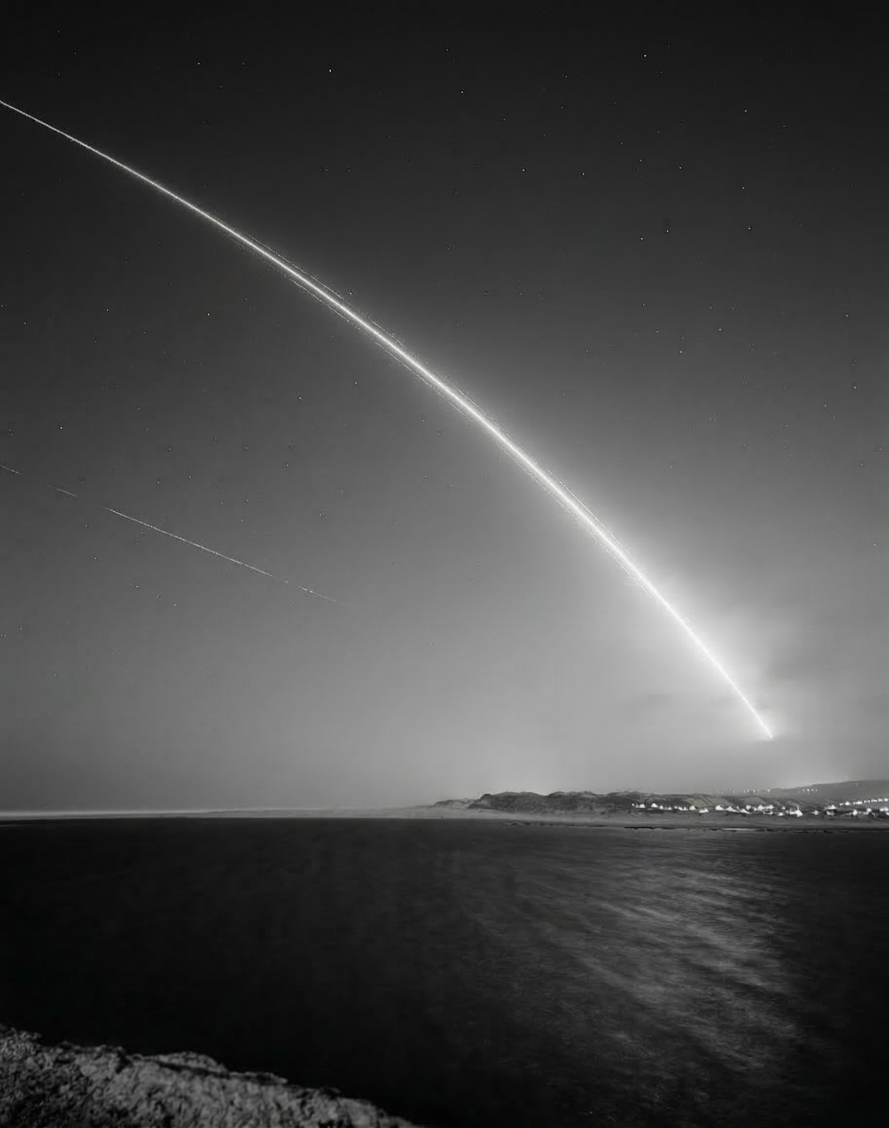 Monochrome coastal night sky with a bright descending arc over the sea